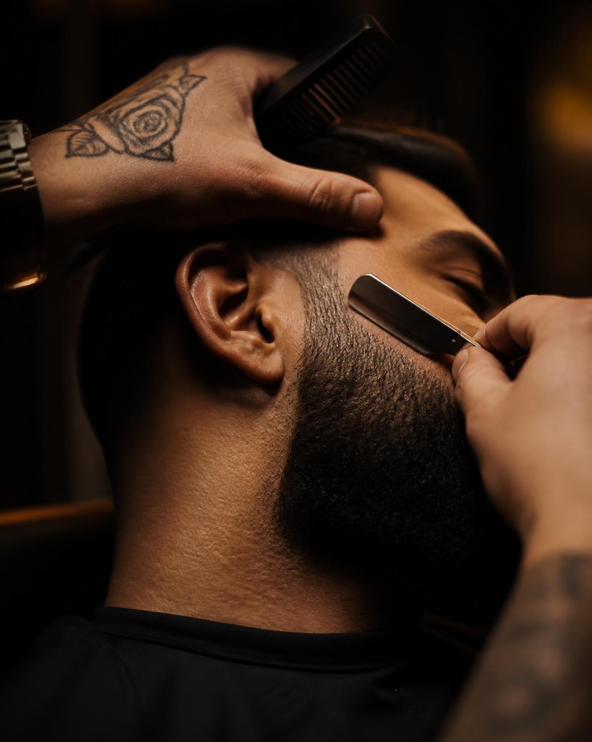 Barber shaping a client's beard with a straight razor and comb